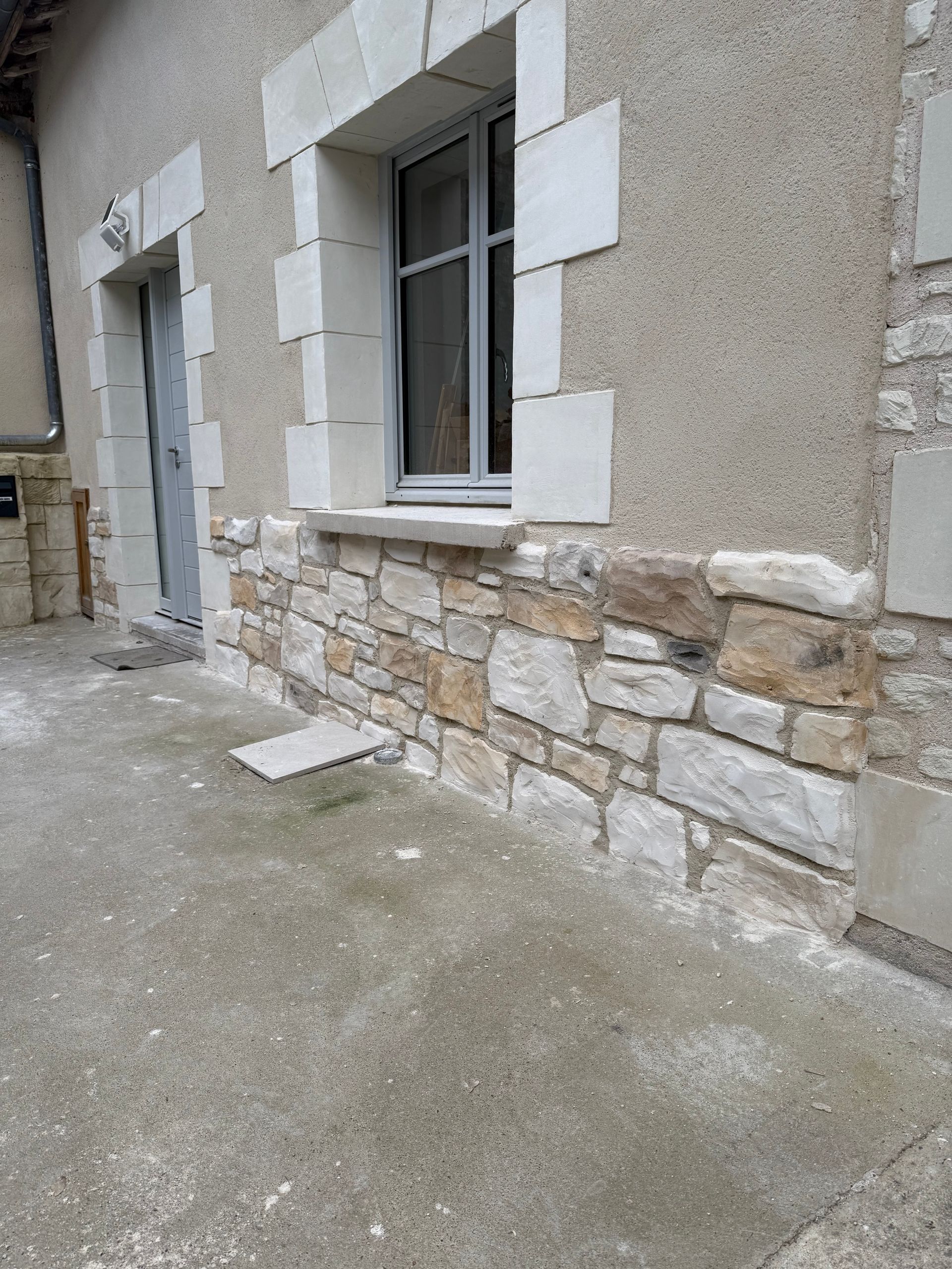 Extérieur d'un bâtiment avec façade en pierre, fenêtre, porte et murs en stuc clair.