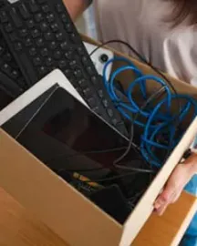Boîte en carton contenant du matériel informatique, dont un écran ou une tablette, un clavier et des câbles électriques enroulés.