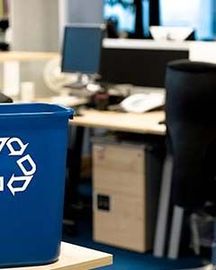 Poubelle de tri bleue avec symbole de recyclage, placée dans un environnement de bureau avec des postes de travail en arrière-plan.