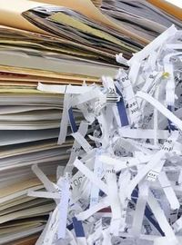 Pile de dossiers et documents papier à côté de bandes de papier déchiquetées issues d’un destructeur de documents.