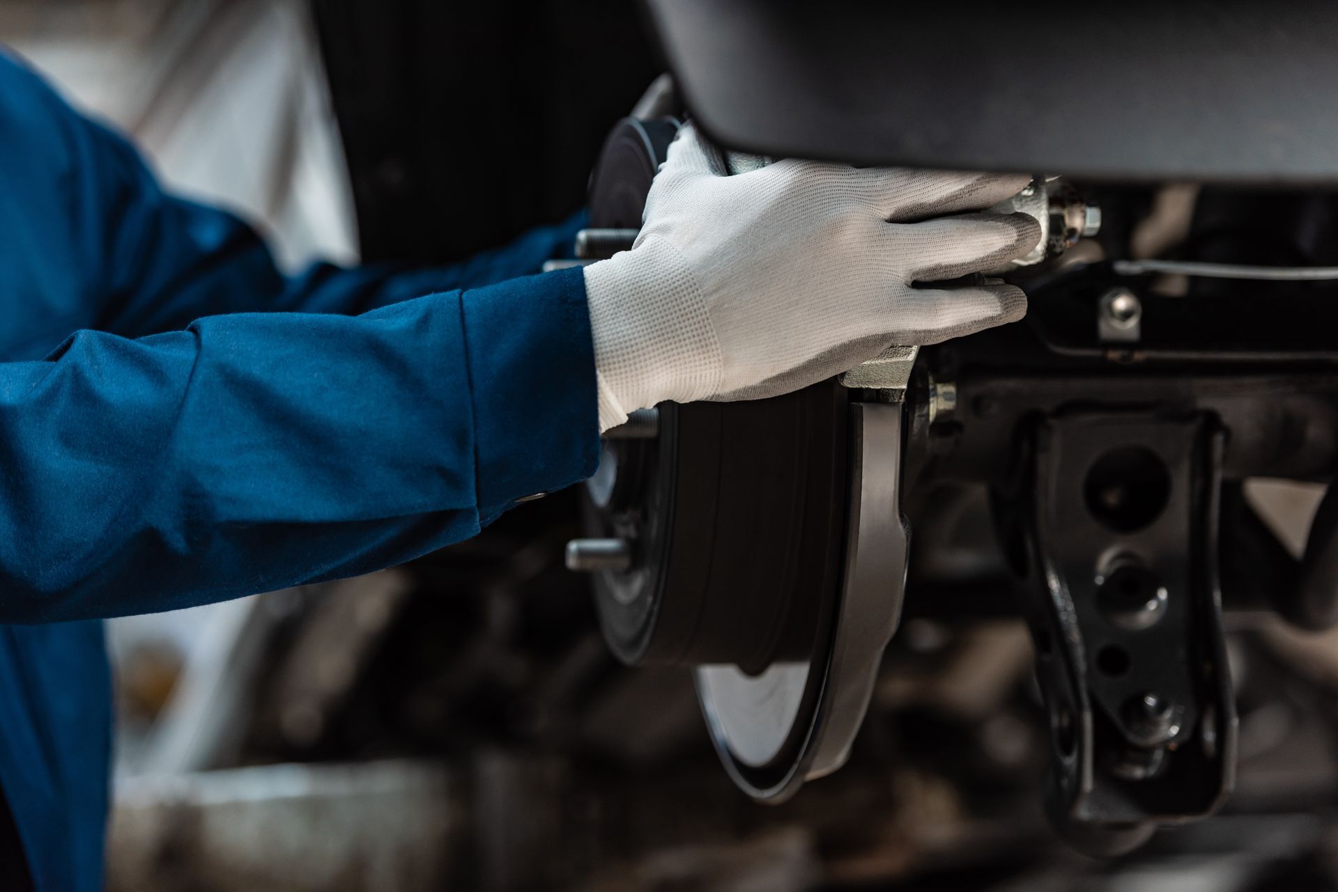 Un mécanicien en uniforme bleu et gants blancs inspecte le système de freinage d'un véhicule.