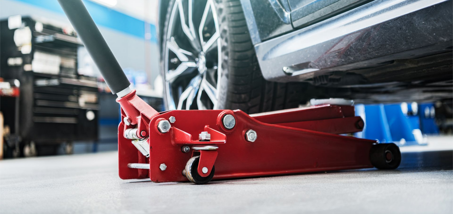 Un cric hydraulique rouge positionné sur un sol sous le côté d'une voiture dans un garage.