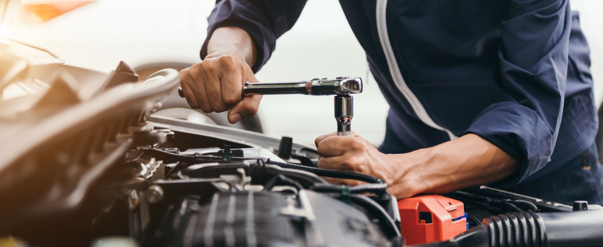 Un mécanicien en uniforme bleu utilise une clé à cliquet pour réparer le moteur d'une voiture.