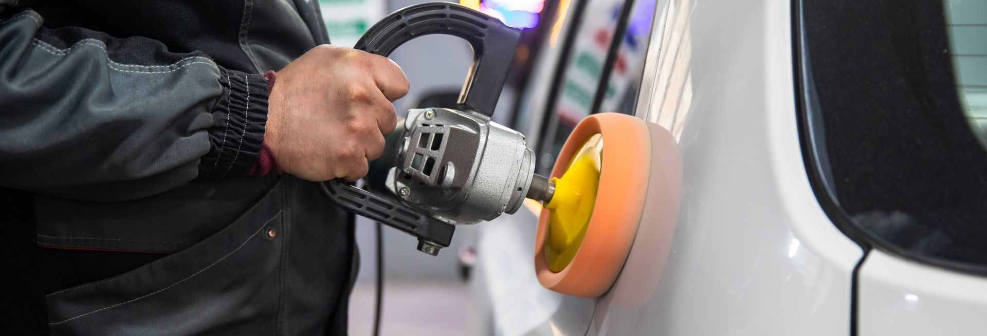 Un ouvrier utilise une polisseuse électrique avec un tampon orange pour polir le côté d'une voiture.