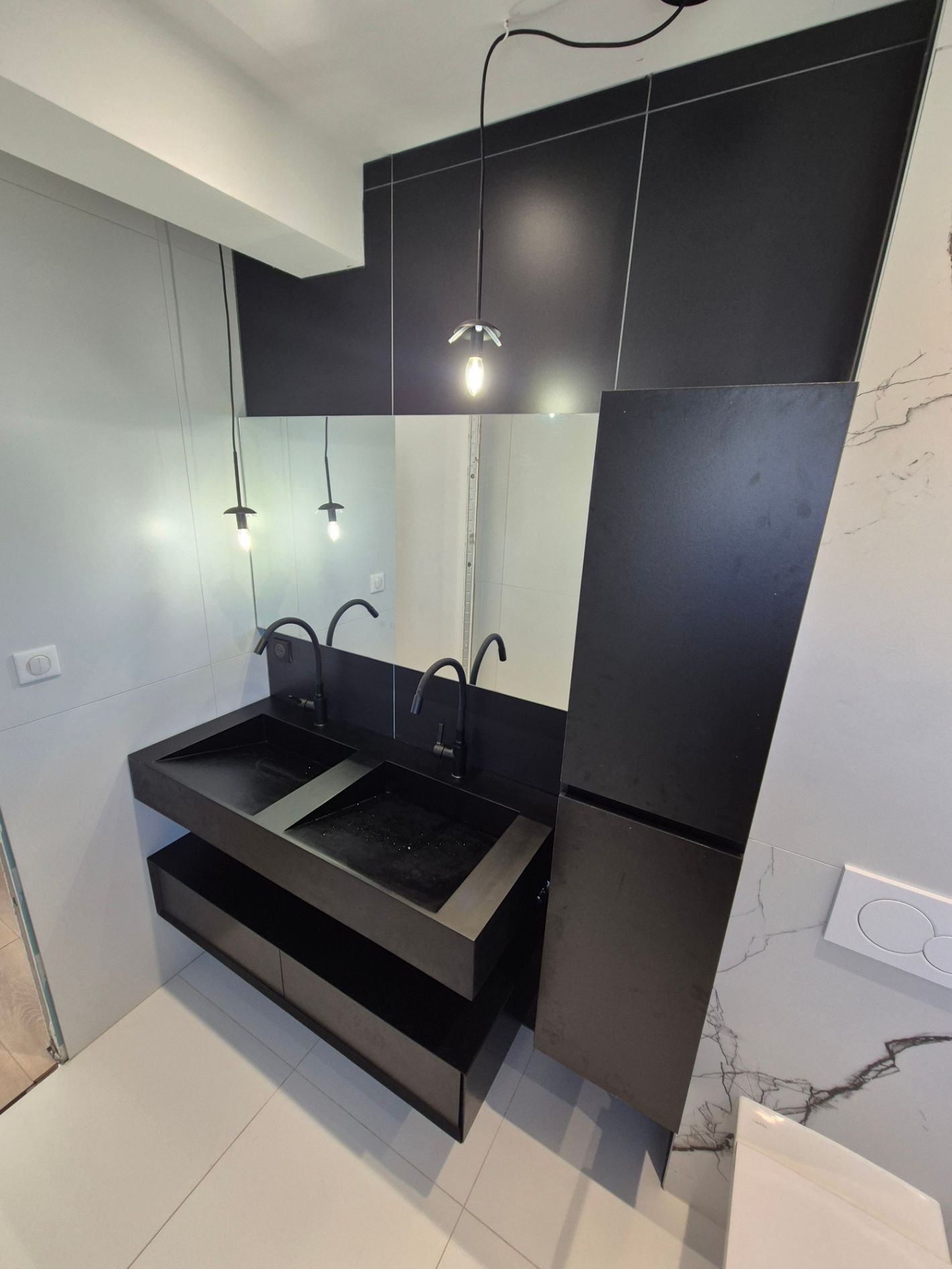 Meuble-lavabo moderne noir à double vasque avec robinetterie noire et suspensions lumineuses dans une salle de bains.