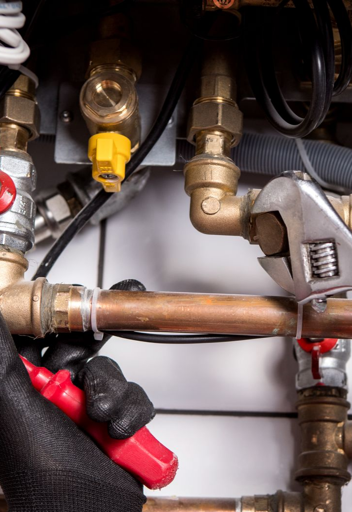 Main gantée de noir, utilisant une clé sur des tuyaux de cuivre et des raccords en laiton.