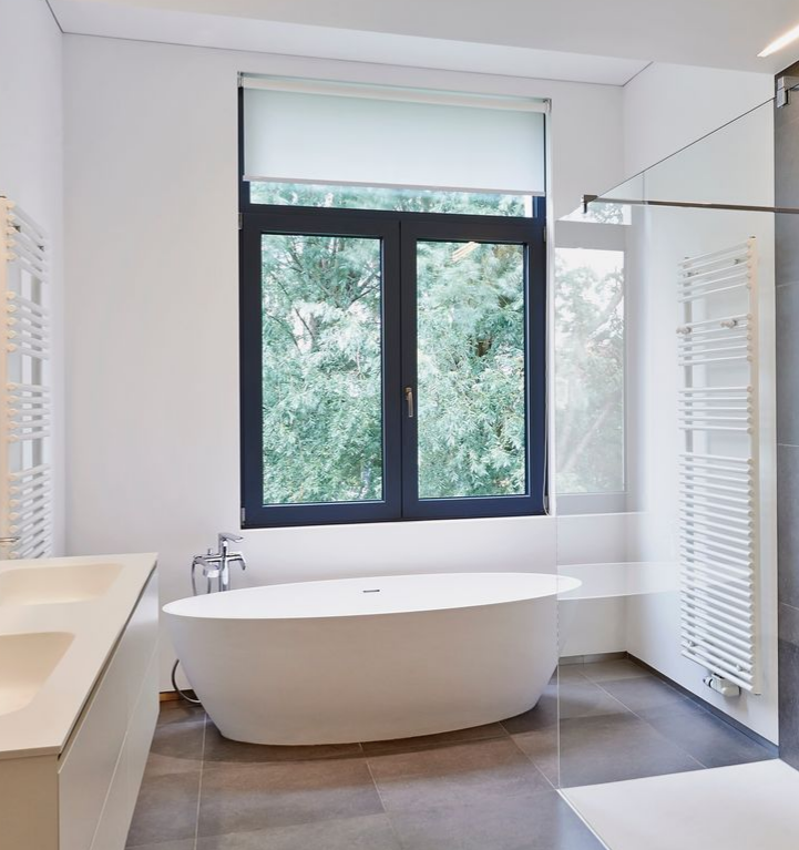 Salle de bains moderne avec baignoire ovale blanche, fenêtre à cadre foncé et sèche-serviettes blanc.