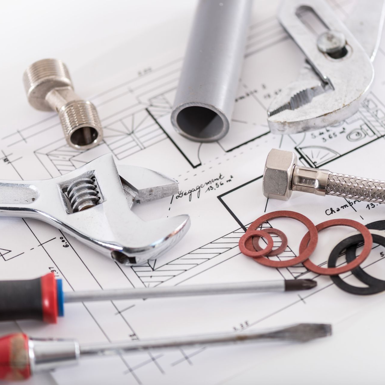 Outils et pièces de plomberie (clés, tuyaux, rondelles) posés sur un plan.