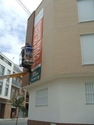 Un hombre está colgando una pancarta en el costado de un edificio.