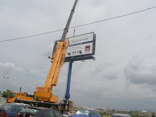 Una gran valla publicitaria está siendo levantada por una grúa.