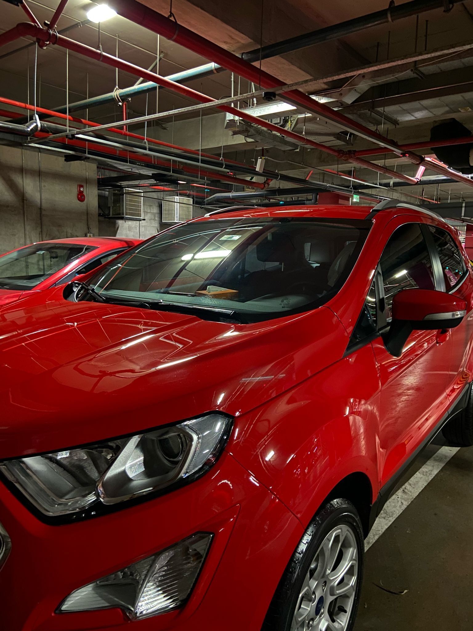 Ford EcoSport rojo estacionado en un estacionamiento interior. Pintura roja brillante, rines cromados y el interior visible a través del parabrisas.