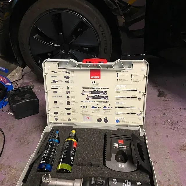 Caja de herramientas abierta con varias herramientas y botellas delante de un neumático de coche negro y una estación de carga.