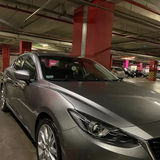Sedán Mazda plateado estacionado en un estacionamiento de varios pisos con columnas rojas.