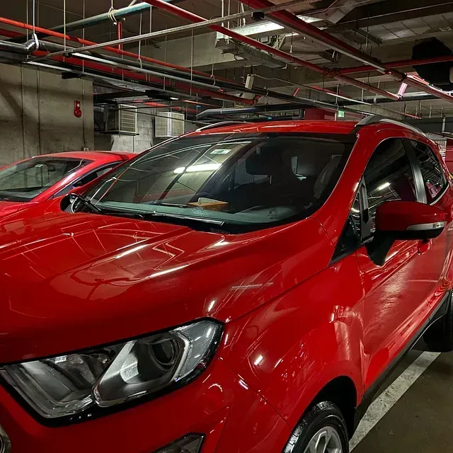 Un Ford EcoSport rojo aparcado en un garaje. Otro coche rojo se ve parcialmente al fondo, bajo una fuerte iluminación.