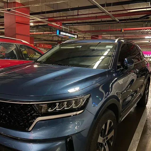 SUV Kia azul estacionado en un estacionamiento interior, con un auto rojo visible a su lado.