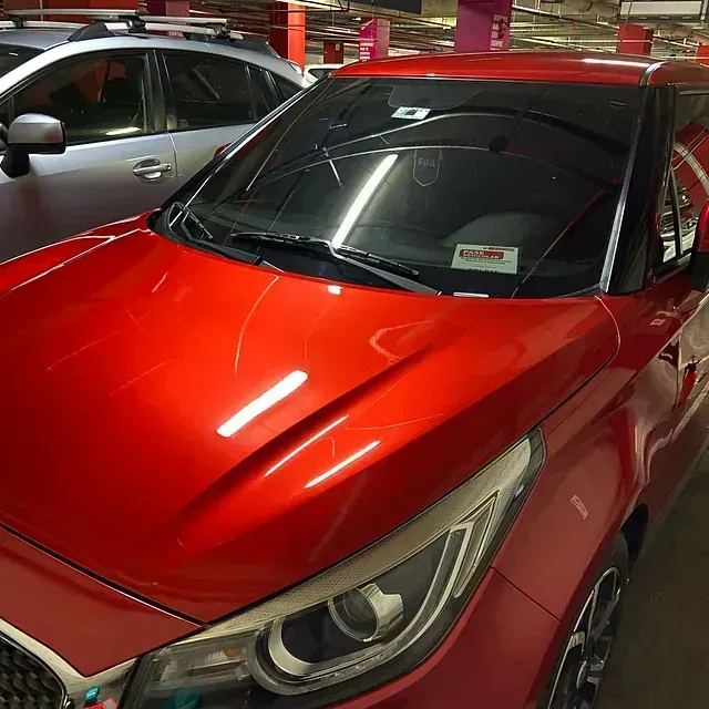 Coche rojo con el parabrisas roto aparcado en un garaje, coche plateado visible al fondo.