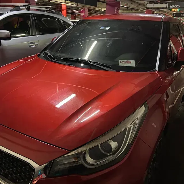 Coche rojo en un aparcamiento con arañazos en el capó y el parabrisas.