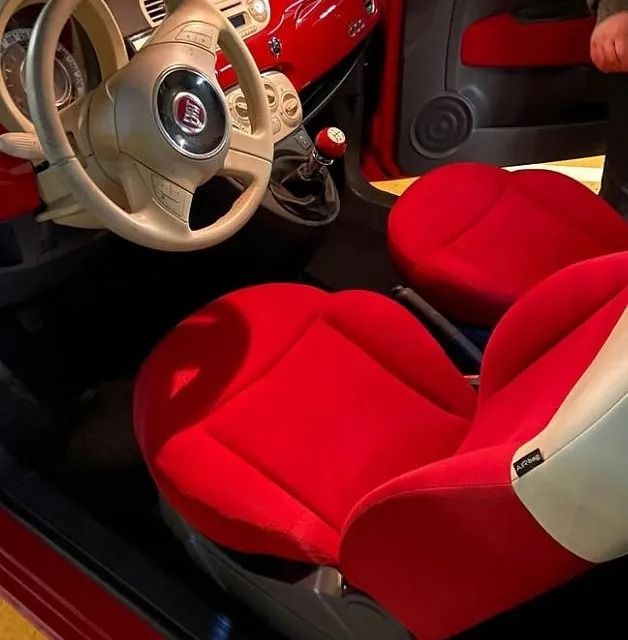 Interior rojo de un automóvil Fiat 500, con asientos rojos, un volante color canela y detalles en el tablero de instrumentos en rojo.
