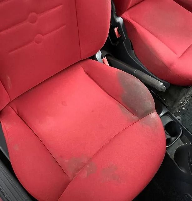 Asiento rojo con manchas visibles. Al observar la base del asiento, se observa decoloración y suciedad, lo que indica desgaste.
