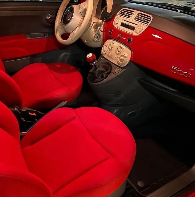 Interior rojo de un Fiat 500 con asientos, tablero y paneles de puertas rojos, volante y consola central de color beige.