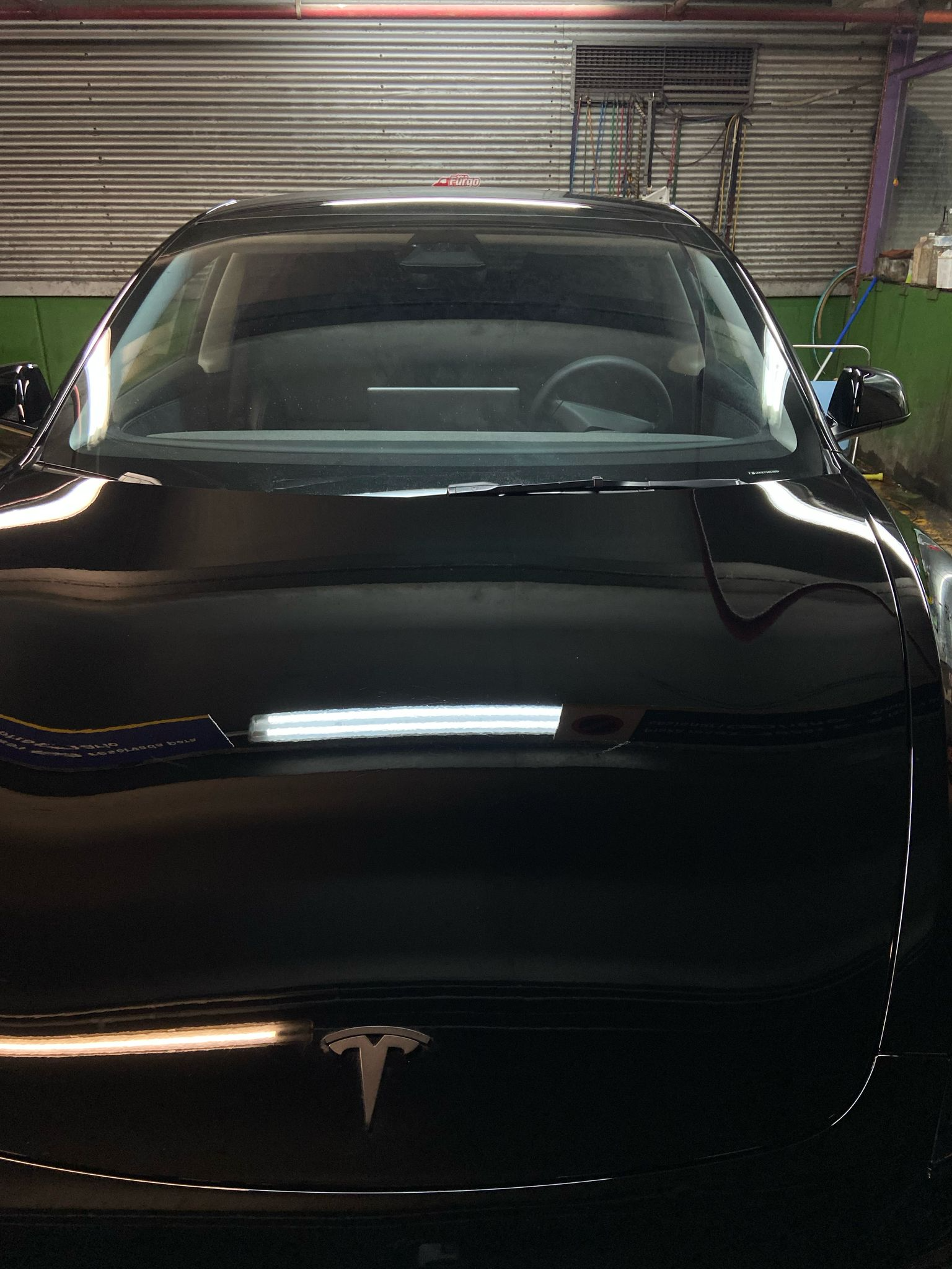 Tesla negro aparcado en un garaje, visto de frente. Se ve el logotipo de Tesla.