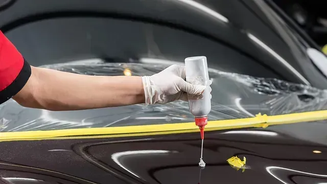 Persona con guantes aplicando líquido de una botella a la carrocería de un automóvil, cubierto con cinta adhesiva.
