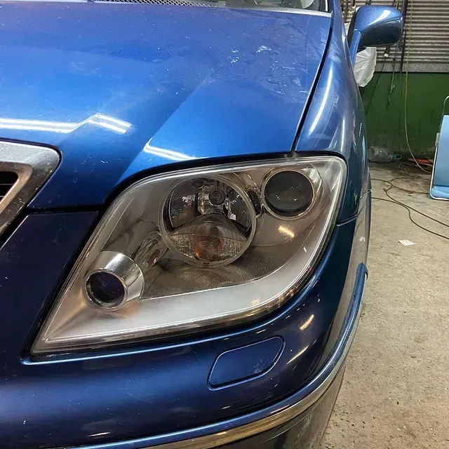 Primer plano del faro de un coche azul. El faro es moderno, con molduras cromadas y luz de posición.