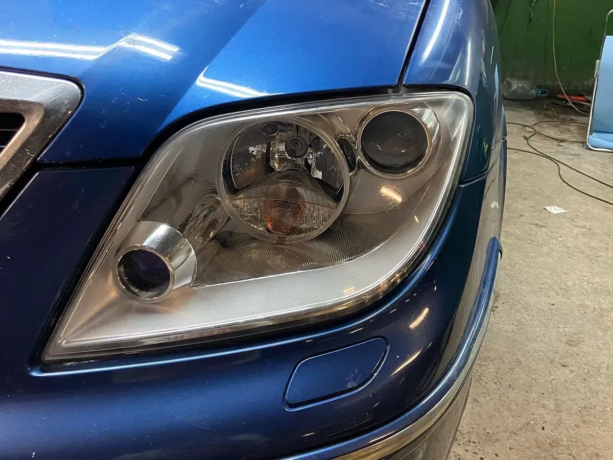 Primer plano del faro de un coche azul. El faro tiene un diseño complejo con múltiples lentes y un borde plateado.
