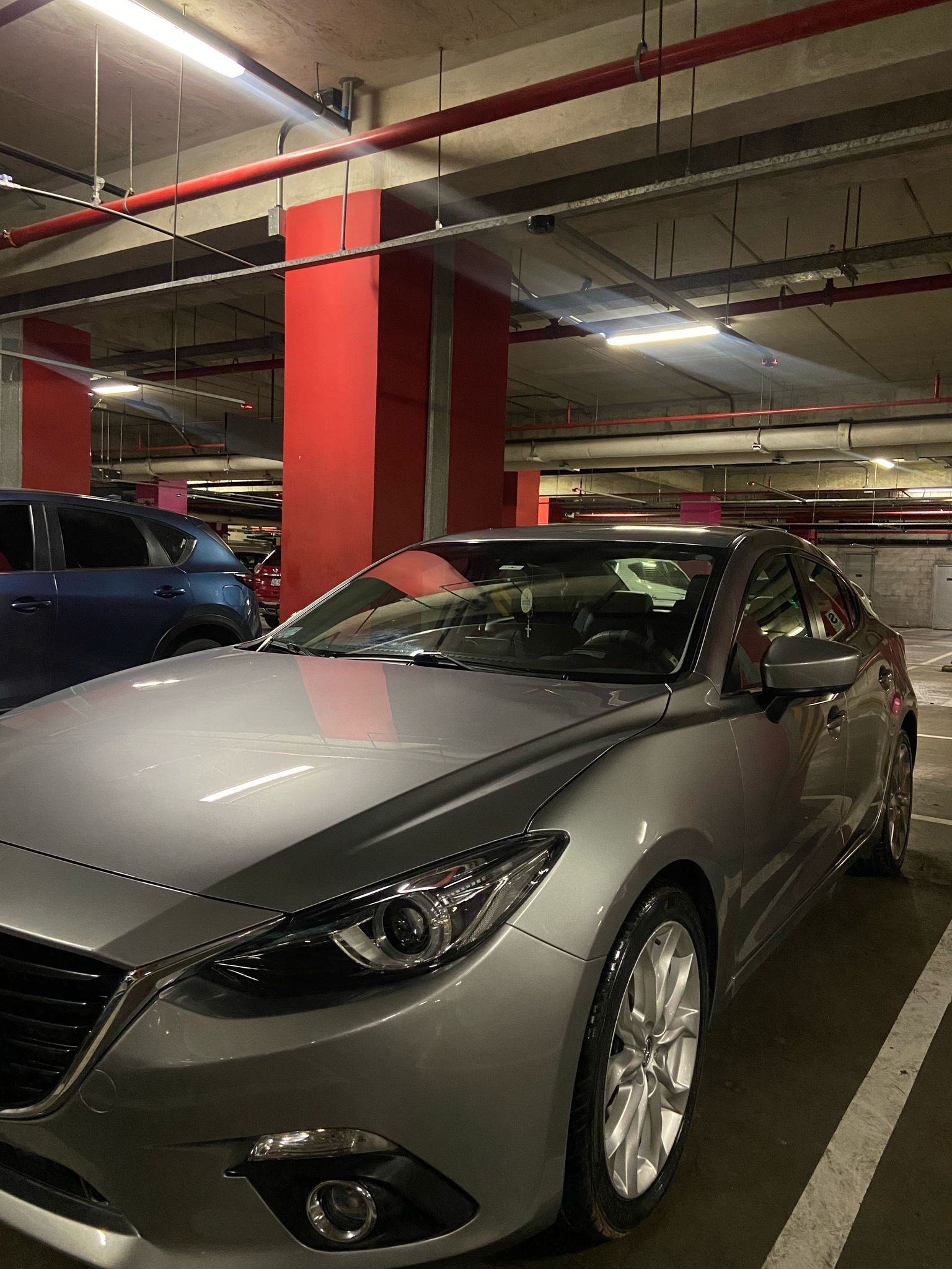 Mazda 3 plateado estacionado en un estacionamiento subterráneo con columnas de soporte rojas.