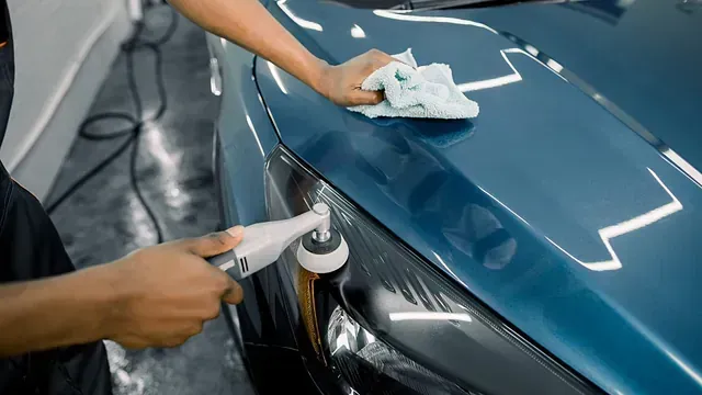 Persona puliendo un faro de coche color verde azulado en un garaje, sosteniendo una pulidora y un paño.
