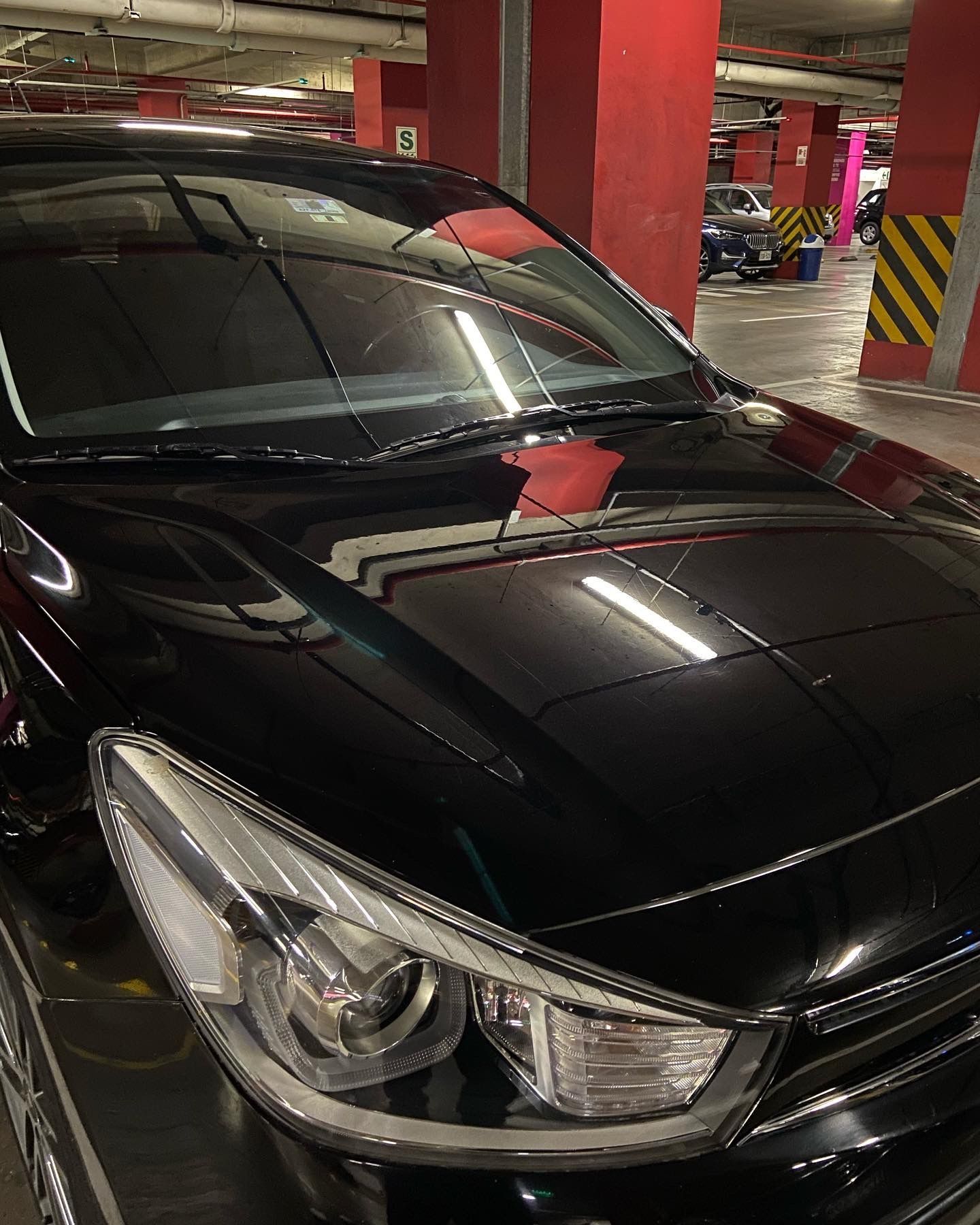 Coche negro aparcado en un aparcamiento interior con columnas rojas y amarillas.