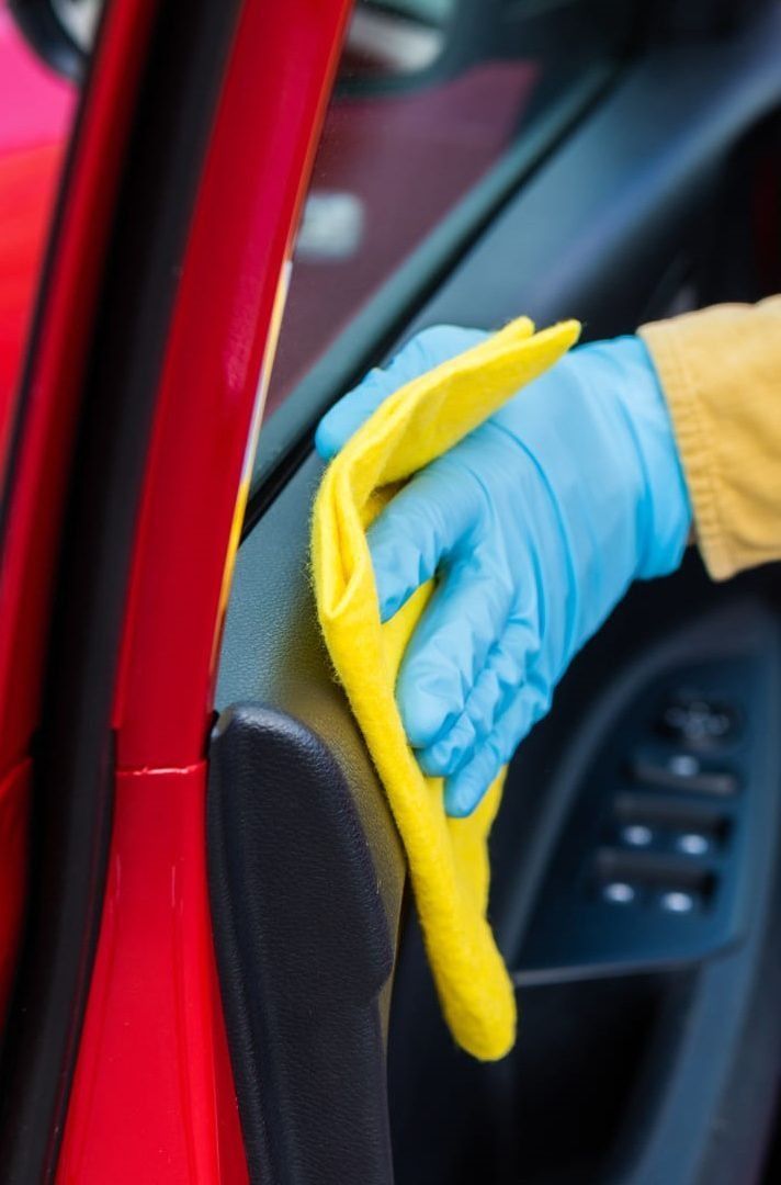 Persona que lleva un guante azul limpia el interior de la puerta de un coche con un paño amarillo.