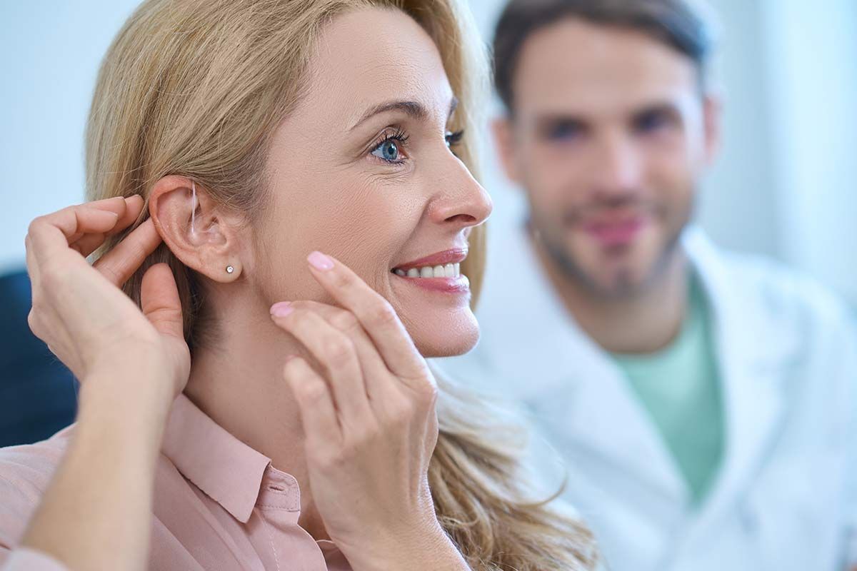 Femme la main derrière l’oreille fixant son appareil auditif