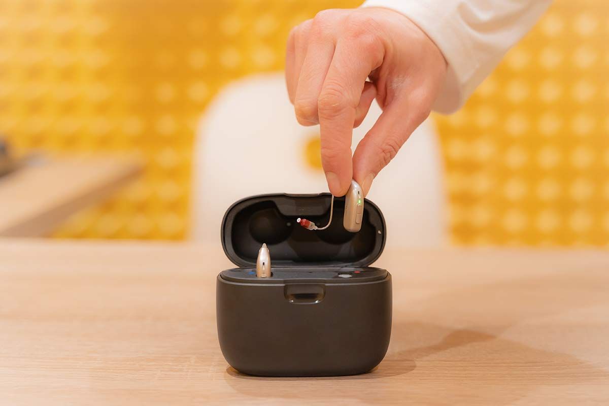 Main qui dépose un appareil auditif dans son boîtier de chargement