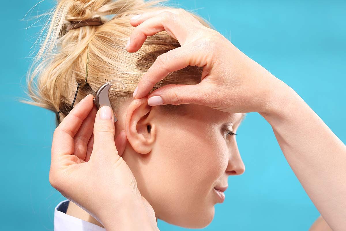 Paire de mains manipule l'appareil auditif d'une femme