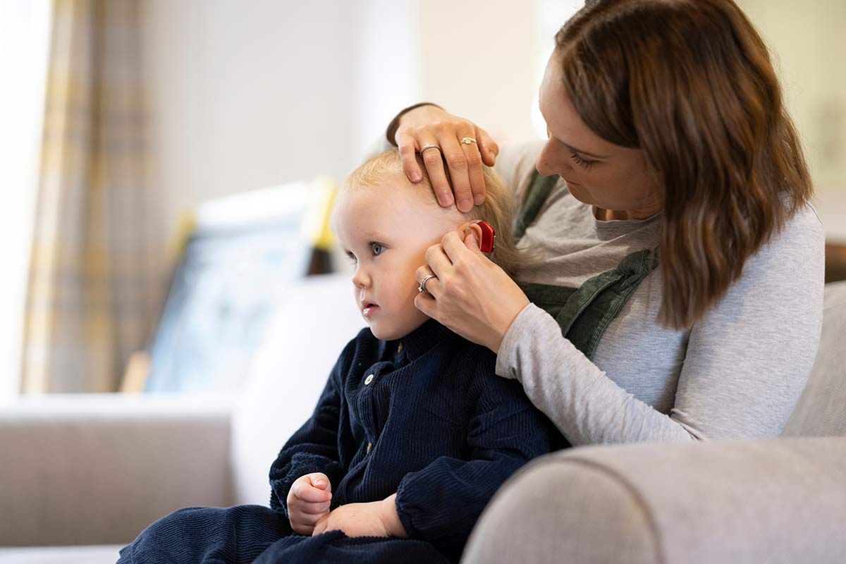 Femme règle l'appareil auditif sur un enfant