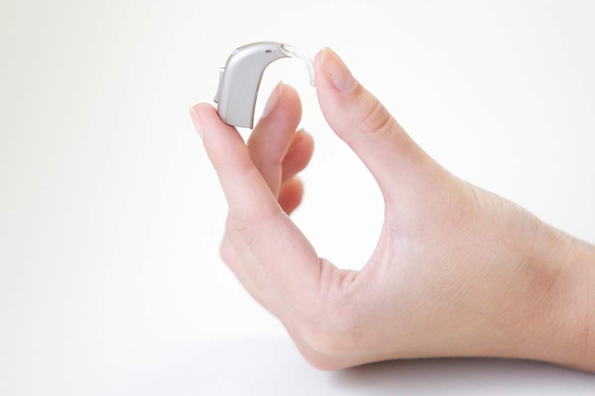 Main qui tient un appareil auditif argenté