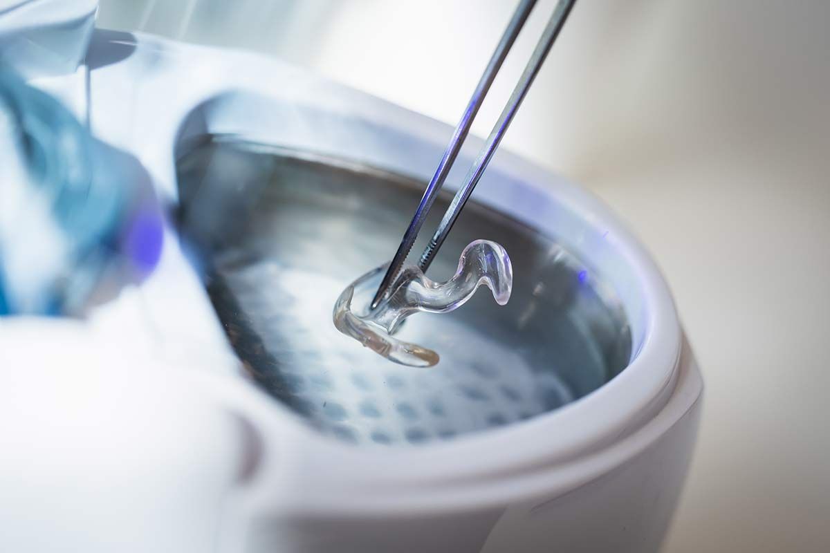 Appareil auditif tenu par précelle pour être nettoyé dans une bassine