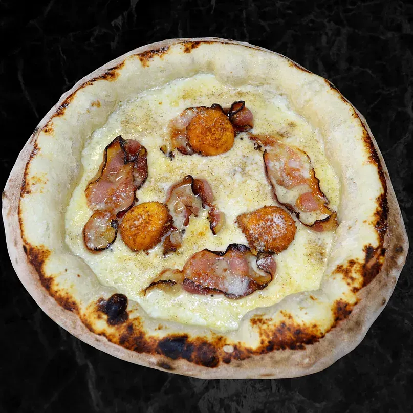 Una pizza con tocino y queso encima está sobre una mesa.