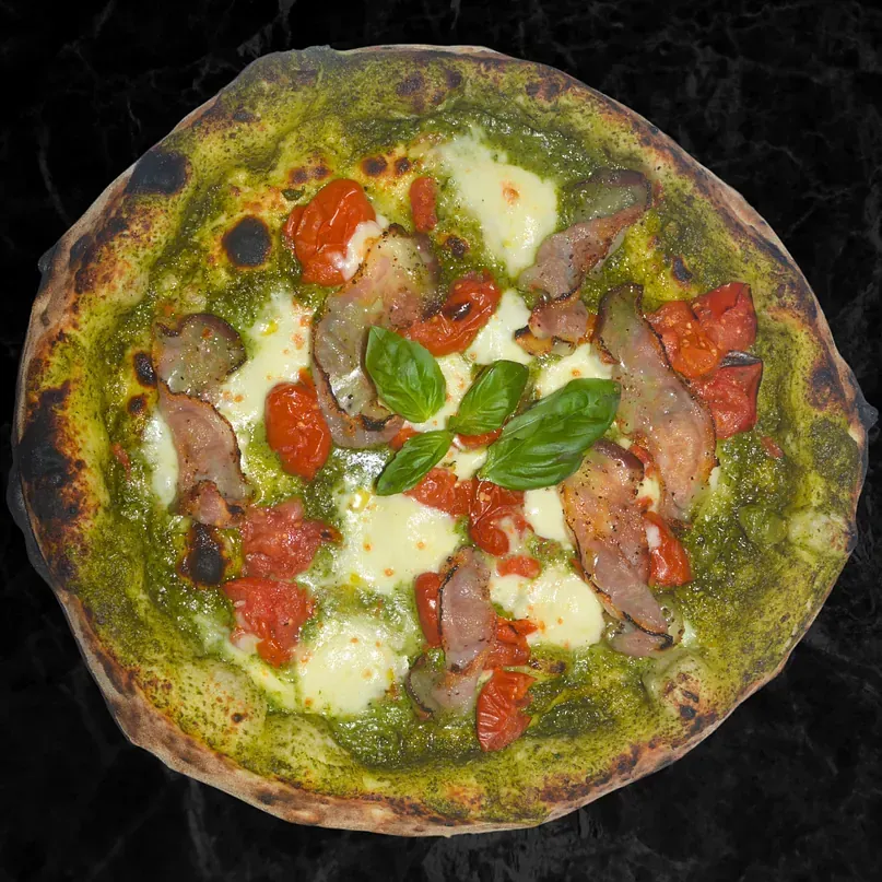 Una pizza con salsa verde y tomates encima.