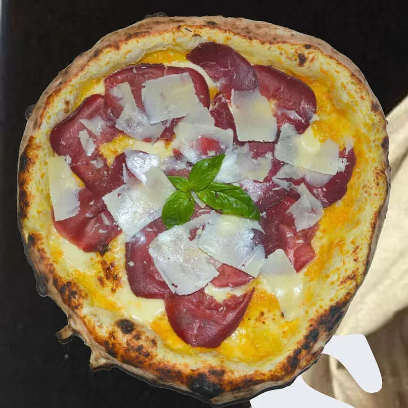Una pizza con carne y queso encima está sobre una mesa.