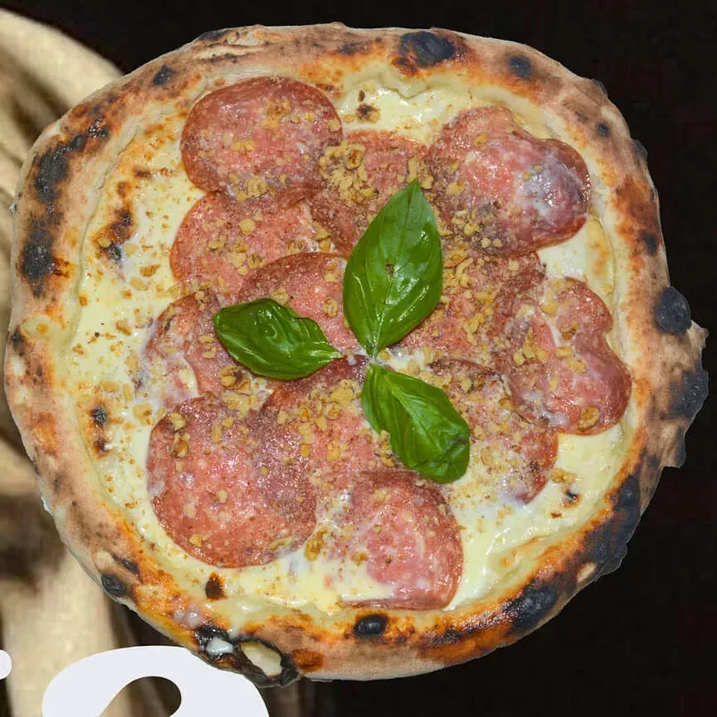 Una pizza con salami y albahaca encima.