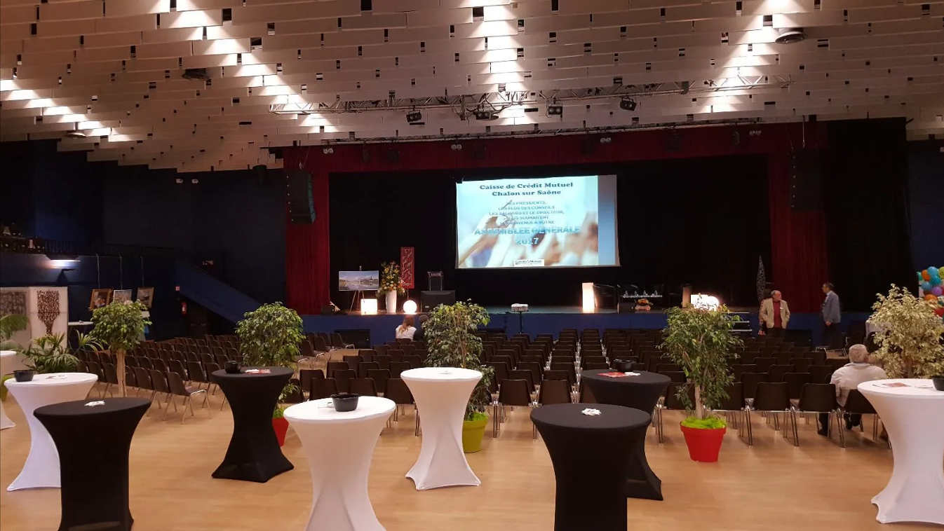 Une salle d'événements avec des tables, des chaises, une scène avec un écran.