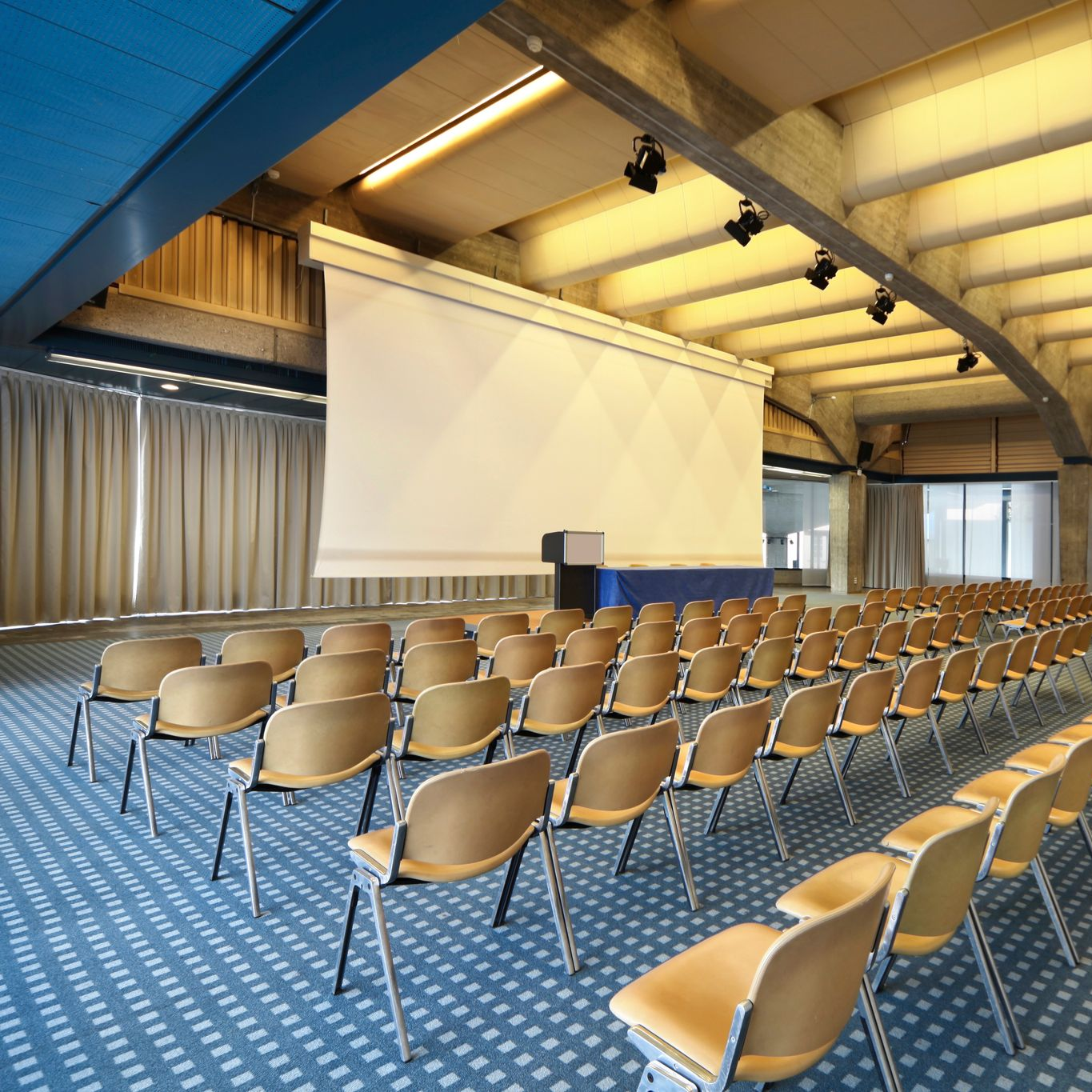 Auditorium avec des rangées de chaises beiges face à un écran.