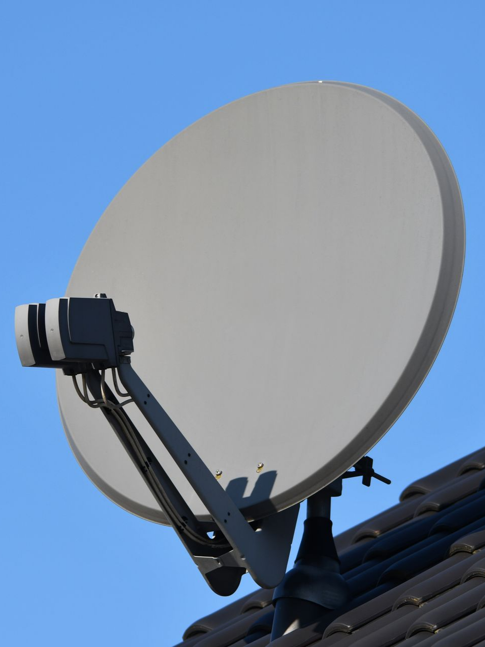 Antenne parabolique montée sur un toit et un ciel bleu.