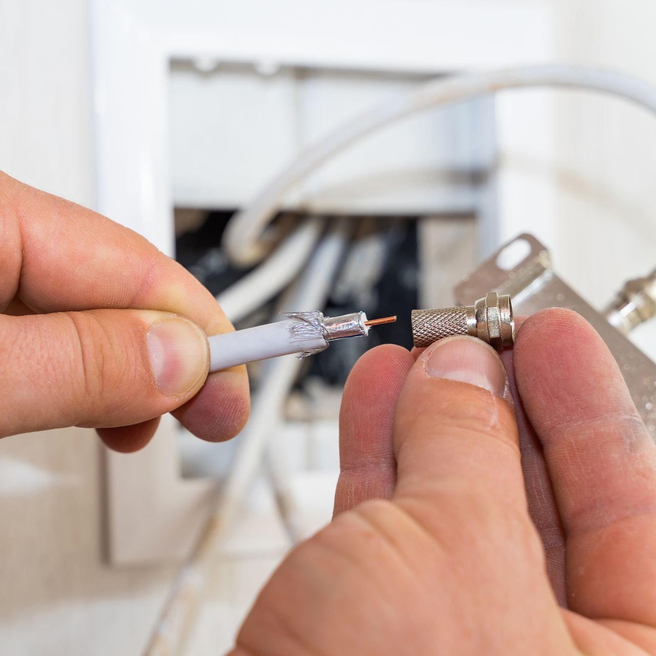 Mains connectant un câble coaxial à un répartiteur de câble à l'intérieur d'un mur.