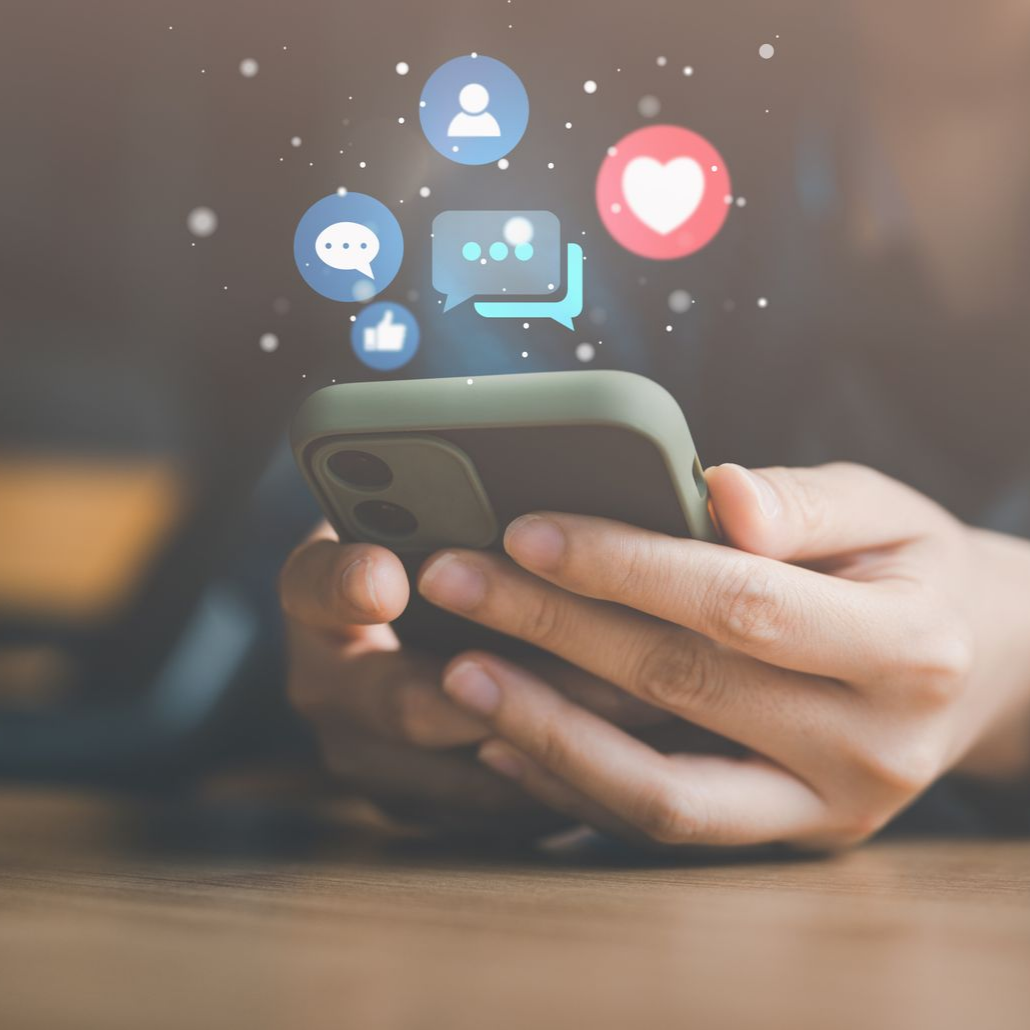 Personne tenant un smartphone avec des  icônes de réseaux sociaux flottant au-dessus.