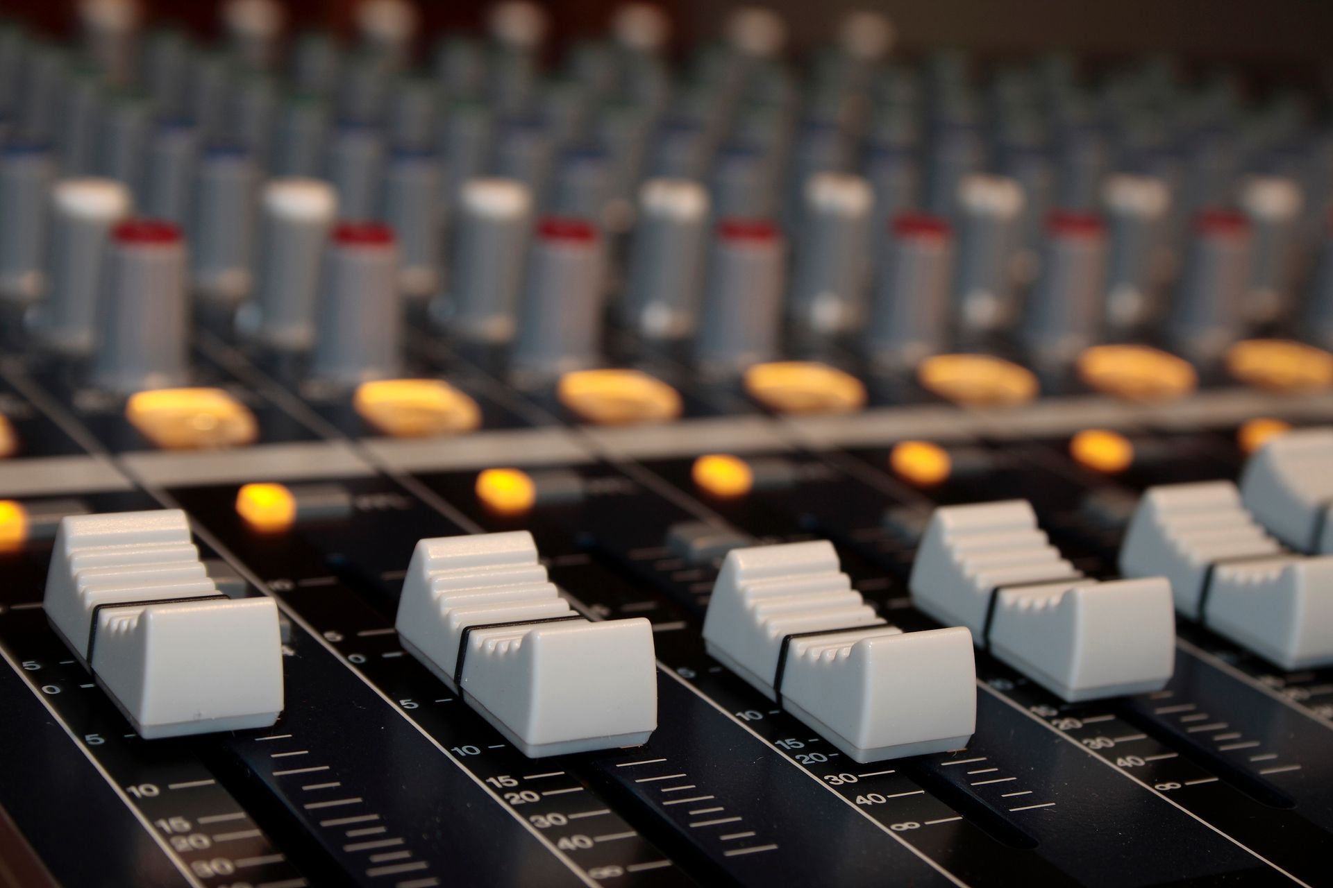 Gros plan d'une console de mixage sonore avec faders et boutons gris.