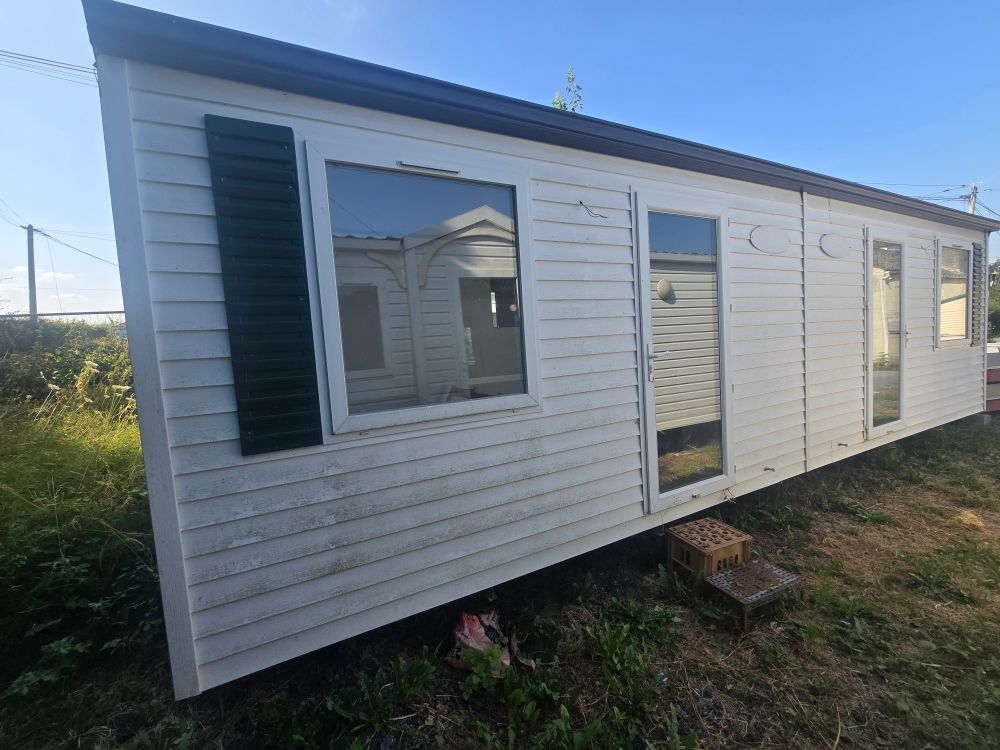 Maison mobile blanche avec volets foncés, porte d'entrée et fenêtres sur un terrain gazonné