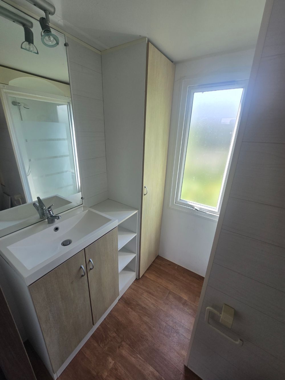 Petite salle de bains avec lavabo, armoire de toilette, étagères de rangement et fenêtre dépolie.